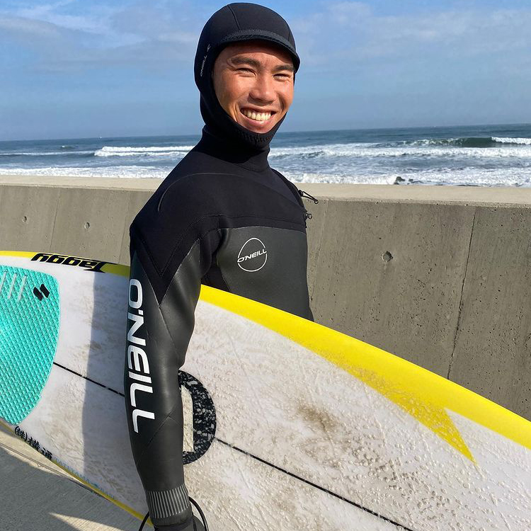 O'NEILL（オニール）チームメンバー HIROTO ARAI（あらい ひろと） サーフボード片手に冬の海辺で笑顔